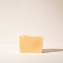 A yellow bar of Lemon Blood Orange soap without wrapping paper on a light background