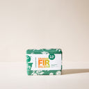 A bar of Orange Fir Balsam wrapped in green paper on a light background.