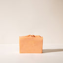 A warm orange bar of Tobacco and Bay Leaf soap without packaging on a light background